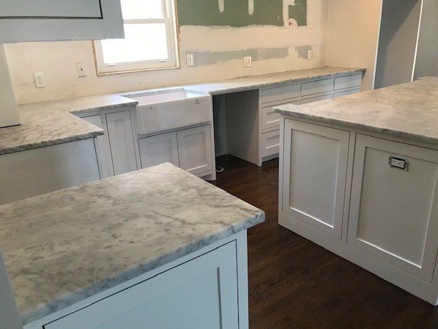 White kitchen with marble countertops and island; under construction.