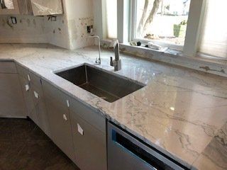 Kitchen countertop with a stainless steel sink and a dishwasher, by a window.