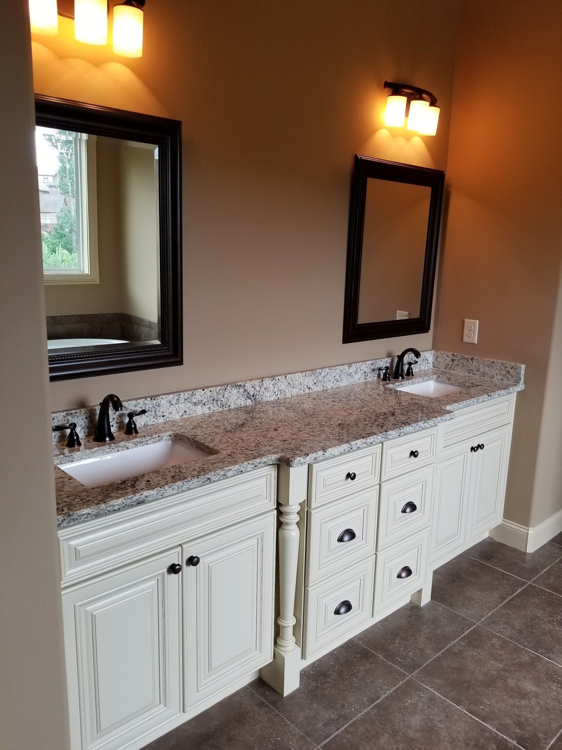 Bathroom with two sinks, white cabinets, granite countertop, black framed mirrors, and beige walls.
