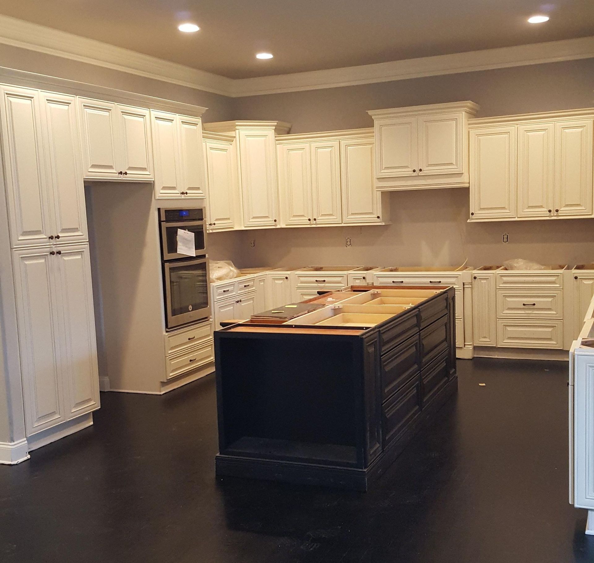 White kitchen cabinets and black island. The kitchen is empty, undergoing construction.