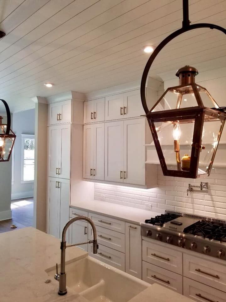 White kitchen with lantern pendants, white cabinets, and a marble countertop.