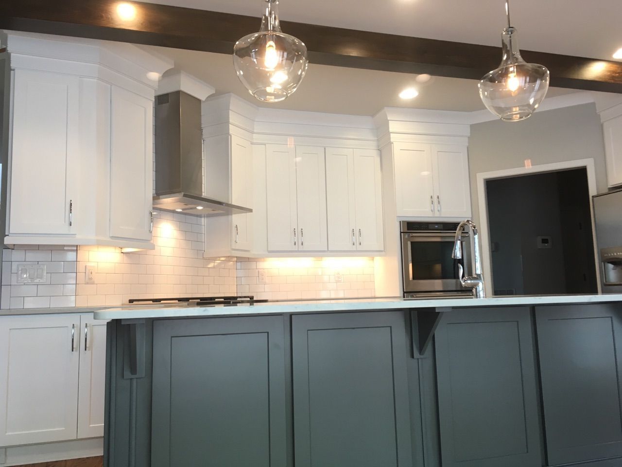 Modern kitchen with white upper cabinets, gray island, stainless steel appliances, and pendant lights.