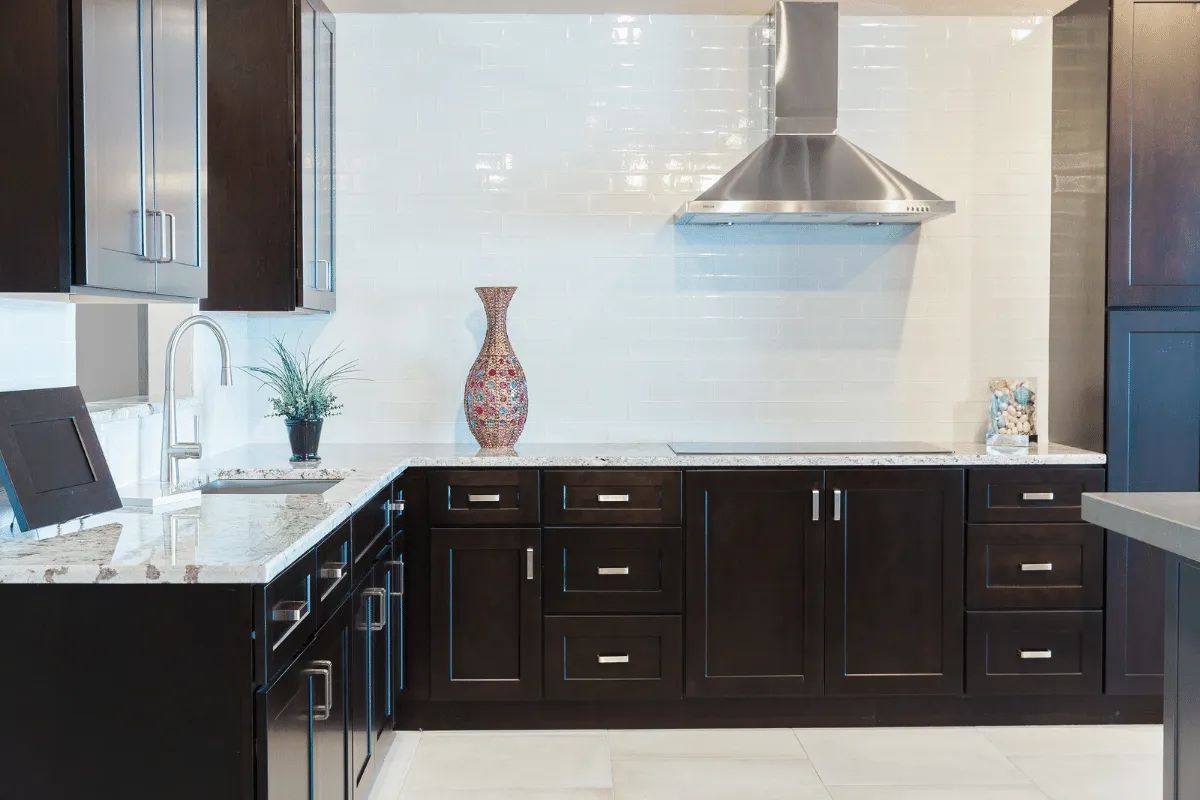 Dark wood kitchen cabinets with white countertops, stainless steel hood, and decorative vase.