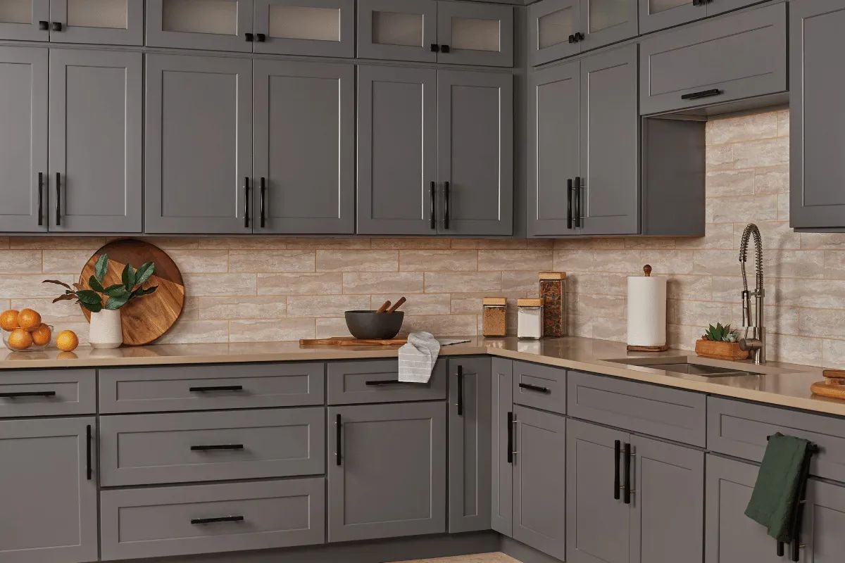 Gray kitchen cabinets with black hardware and a neutral backsplash.
