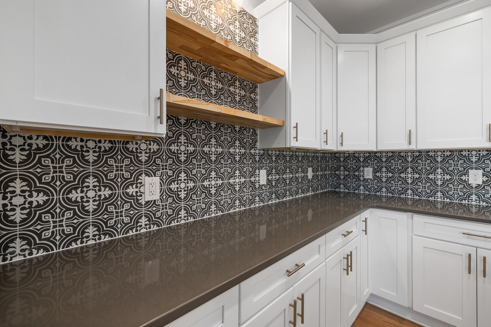 Modern kitchen with white cabinets, dark countertops, and black-and-white patterned backsplash.