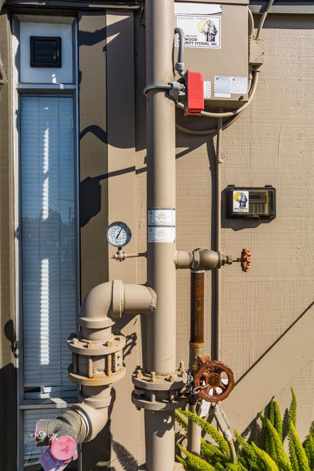 Outdoor utility pipes and meters on a stucco wall beside a blue door and a red electrical box