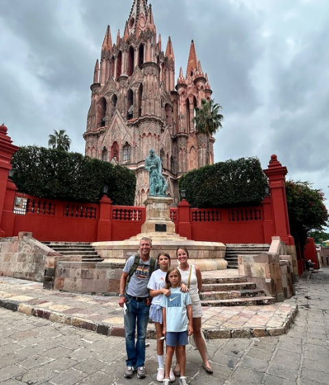 Family posing in front of a red cathedral and statue under cloudy skies