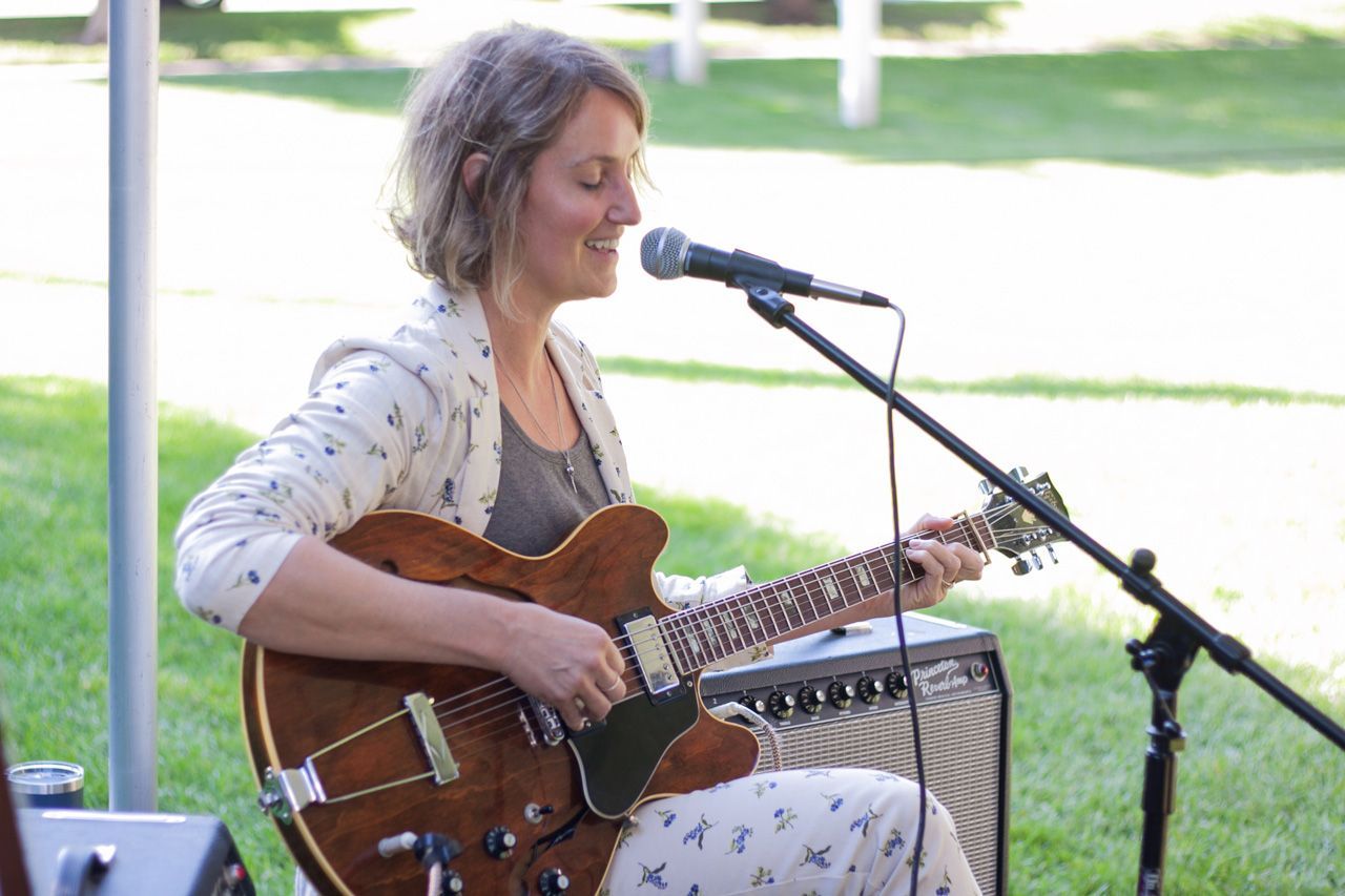 Woman playing a brown electric guitar and singing into a microphone outdoors
