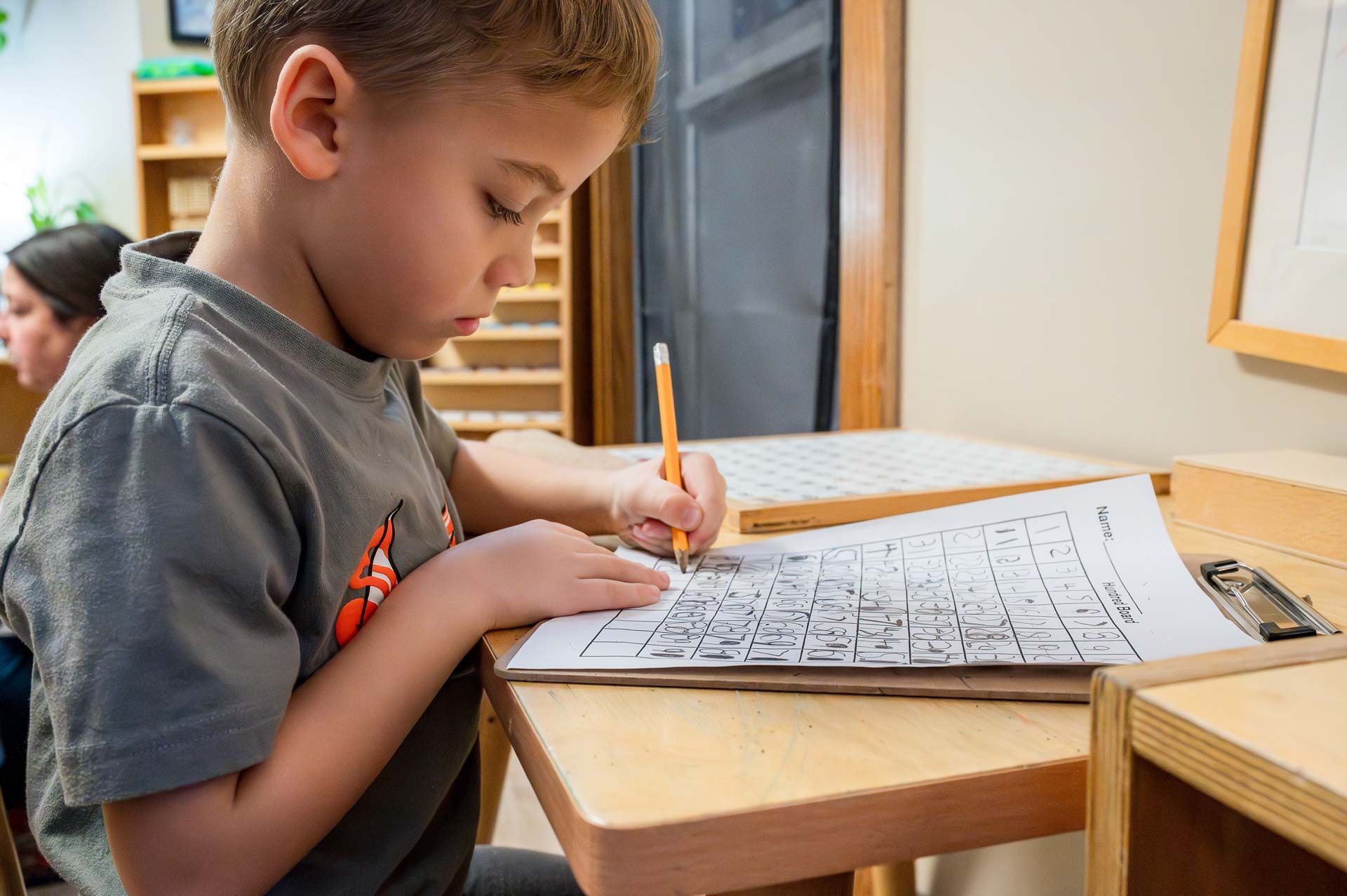 montessori child practicing handwriting at a desk with a clipboard and worksheet