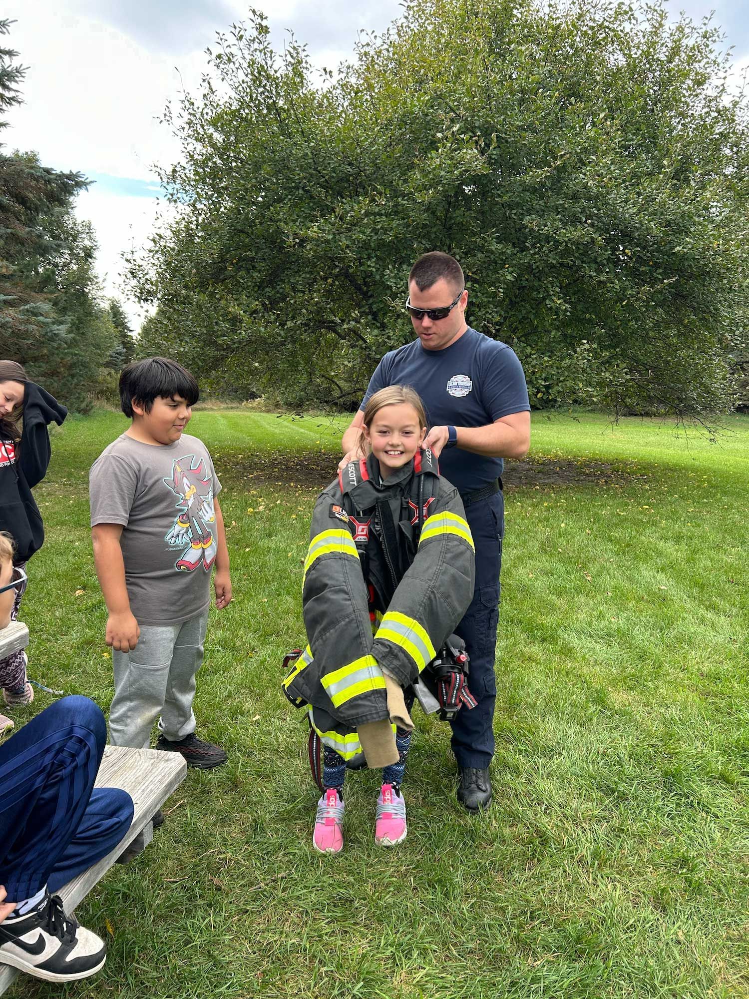 montessori child trying on firefighter gear with firefighter and peers outdoors