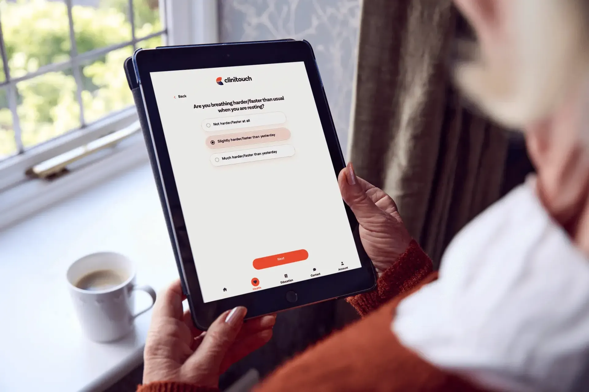 A person is holding a tablet in their hands in front of a window.