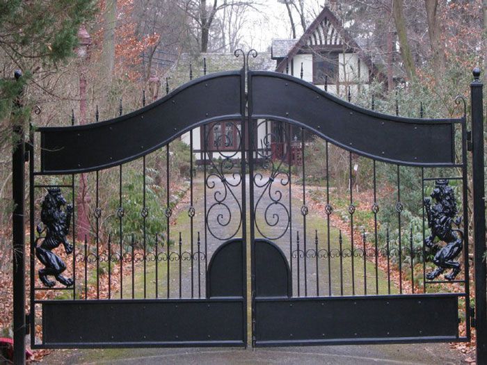 A tall, black metal sliding gate with vertical pickets and spiked finials stands in front of a dark building.