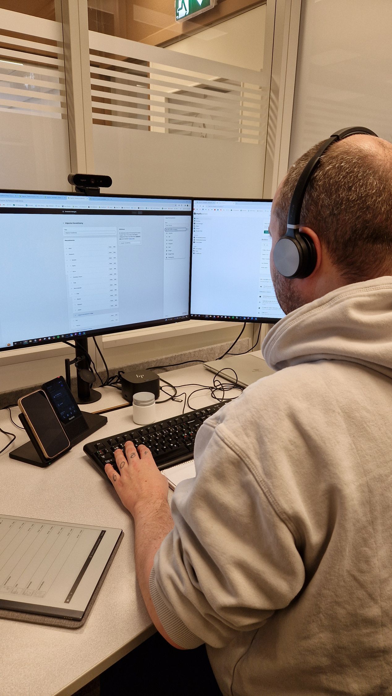 En person med hodetelefoner jobber ved et skrivebord med to skjermer i et kontrollrom.