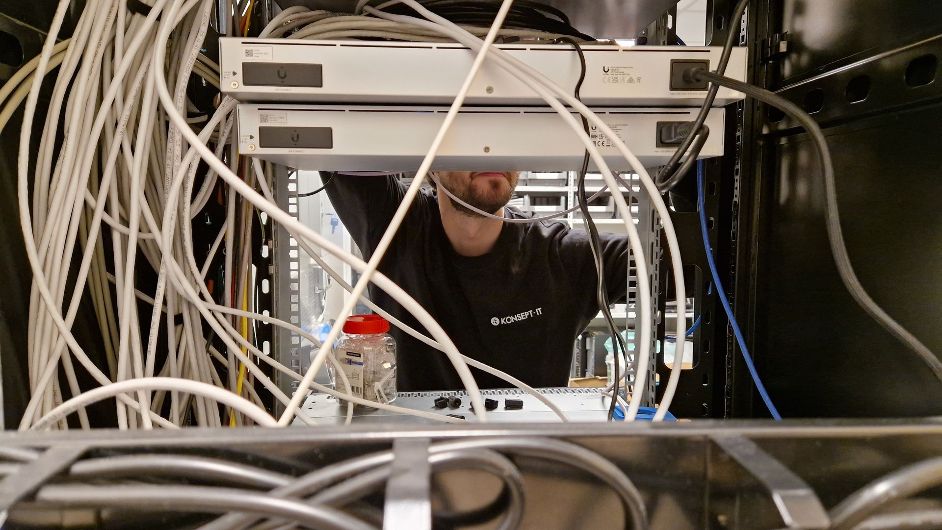 Tekniker som jobber inne i et serverrack omgitt av kabler og nettverksutstyr
