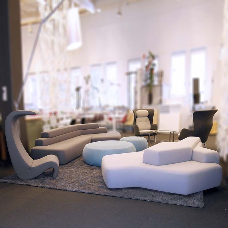 Moderne stue med skulpturelle hvite, grå og blå sofaer på et teppe i et lyst utstillingslokale