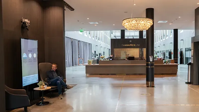 Moderne hotellobby med sitteplasser, resepsjon og en person som bruker en telefon til venstre