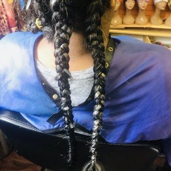 Close-up of two long, gray and black braided hair extensions against a blue salon cape.