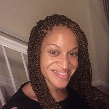 Person with brown braided hair smiling at the camera. Black shirt, indoor setting.