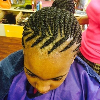 Woman with zig-zag cornrow braids styled in a bun, wearing a purple cape.