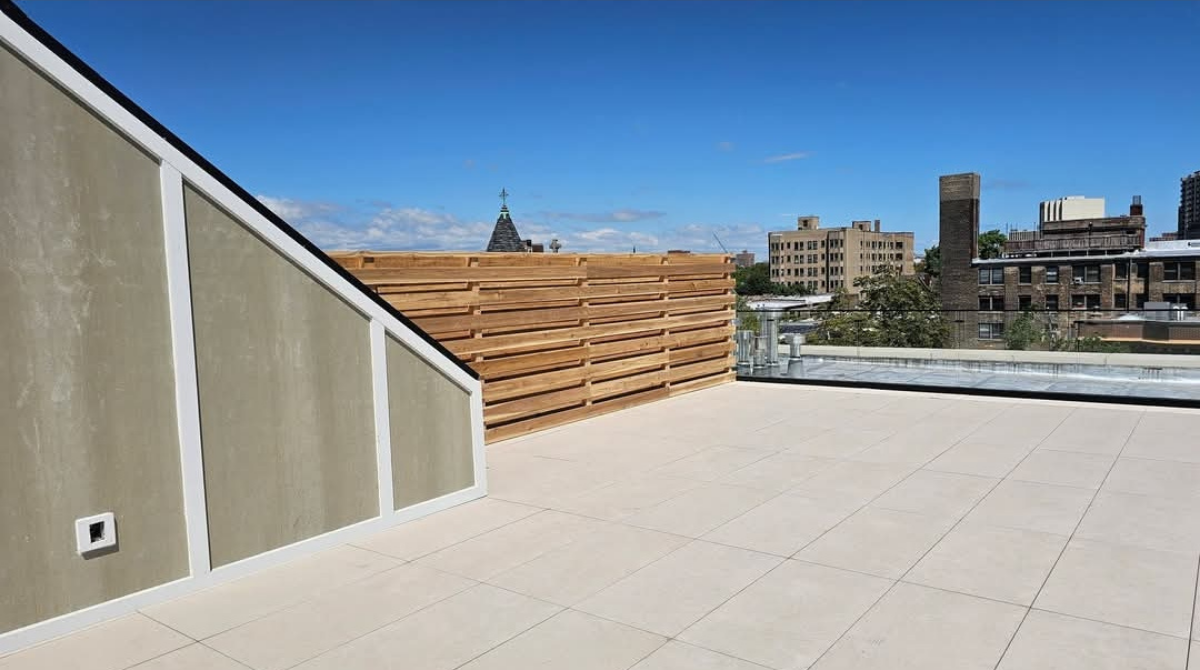 Rooftop terrace with white tiled floor, wood slat wall, and city skyline beyond a glass railing