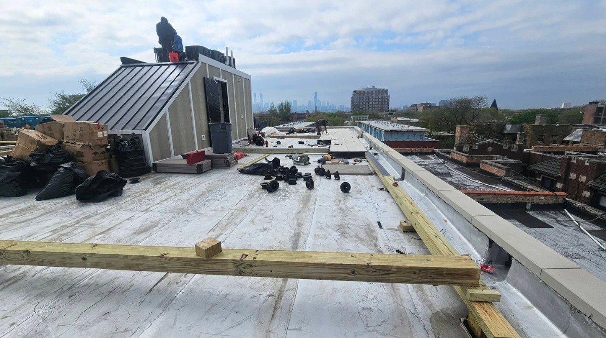 Rooftop under construction with white roofing, scattered materials, and a worker near a metal structure.