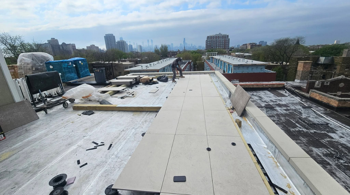 Flat rooftop construction site with white membrane roofing, tools, and materials under a cloudy sky