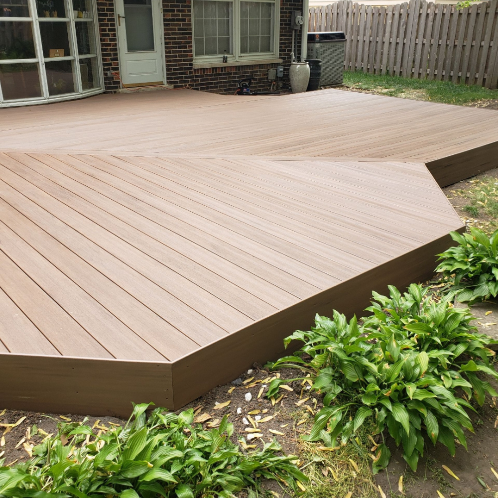 Raised wooden deck patio with curved edge and green shrubs along the front in a backyard.