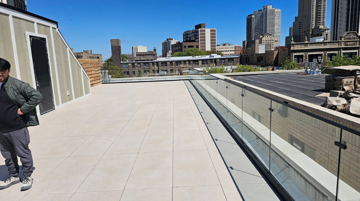 Wide concrete walkway beside modern buildings and water, with a person walking on the left in bright sunlight.
