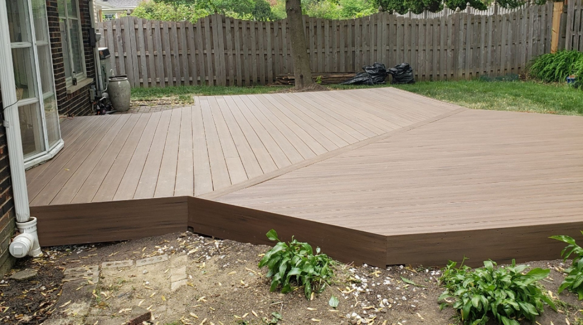Wooden backyard deck with a raised edge and fence in the background