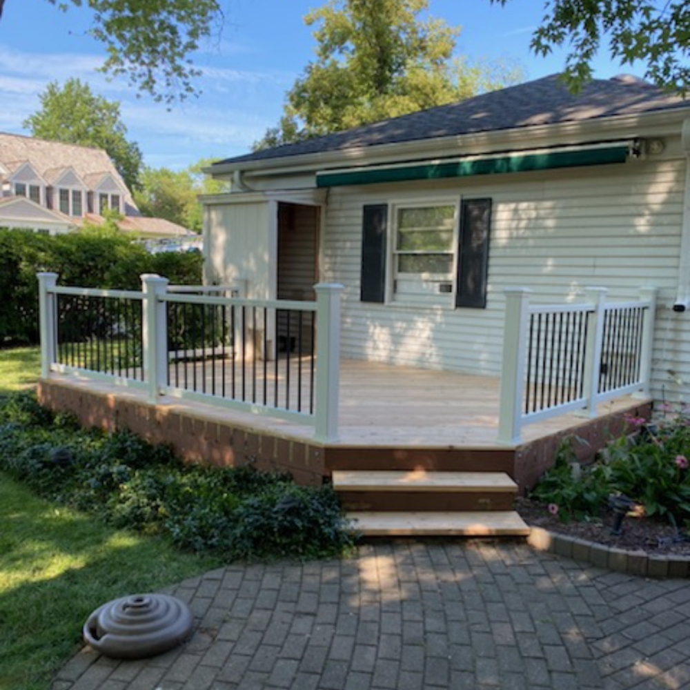 White house porch with railing, steps, and paver patio in a sunny yard