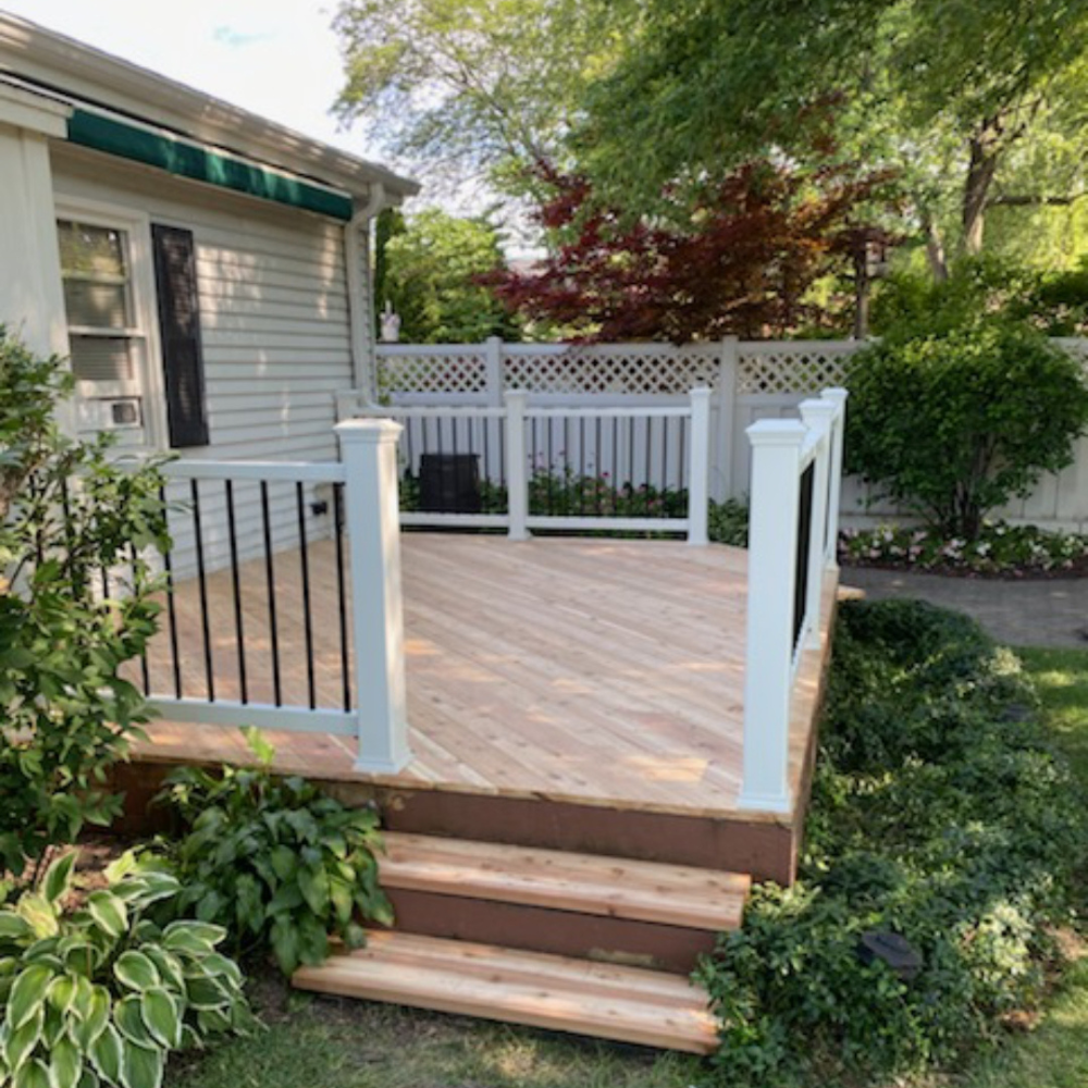 Wooden backyard deck with steps, black railing, and white lattice fence beside a house