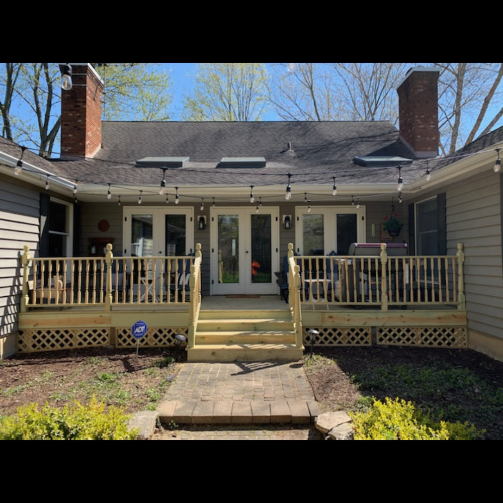 Front porch of a house with wooden railings, central steps, and double glass doors on a sunny day