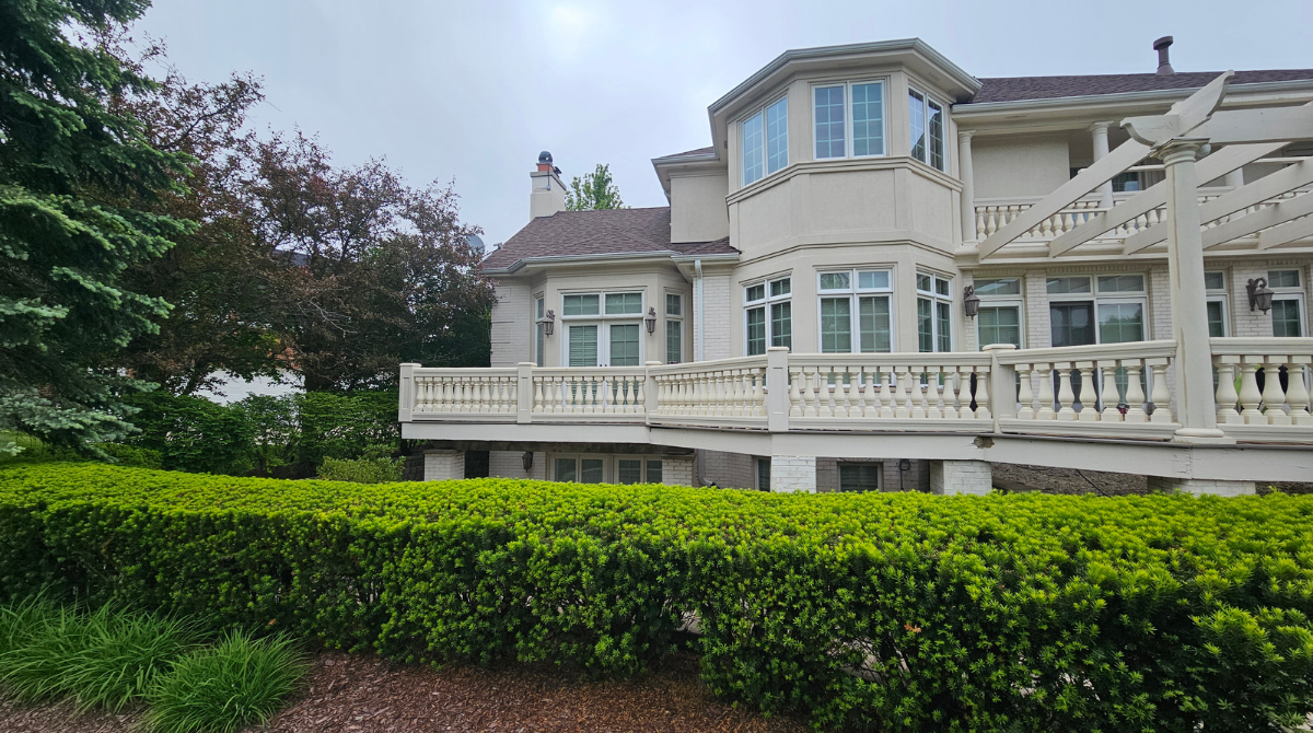 Elegant white mansion with bay windows and a veranda behind a trimmed green hedge
