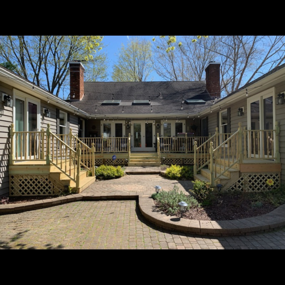 Courtyard patio with brick pavers and beige porches on both sides, framed by trees under a blue sky