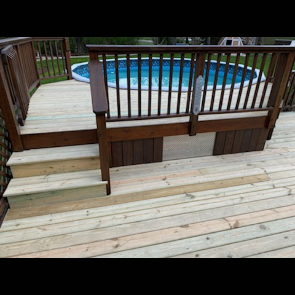 Wooden deck with steps leading to an above-ground pool and brown railing in a backyard