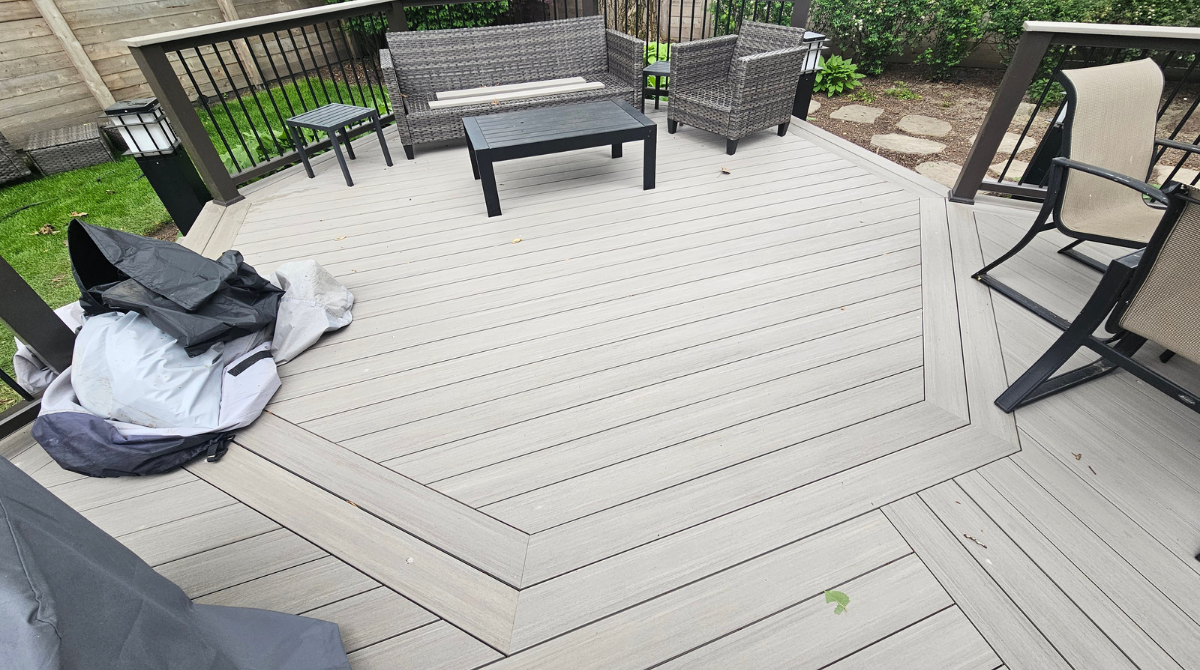 Patio deck with outdoor seating, a grill cover, and a low table near a black railing and potted plants.