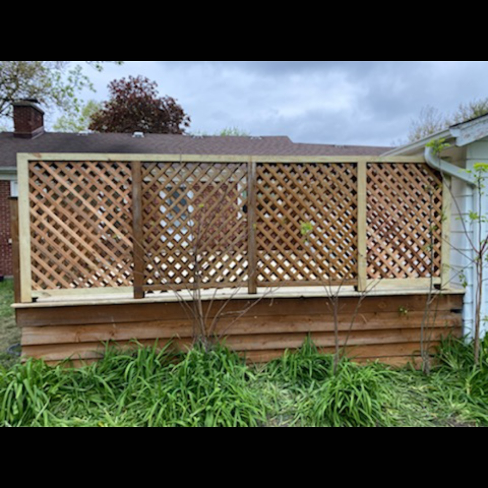 Wooden lattice fence with raised planter boxes and greenery in a backyard under cloudy sky