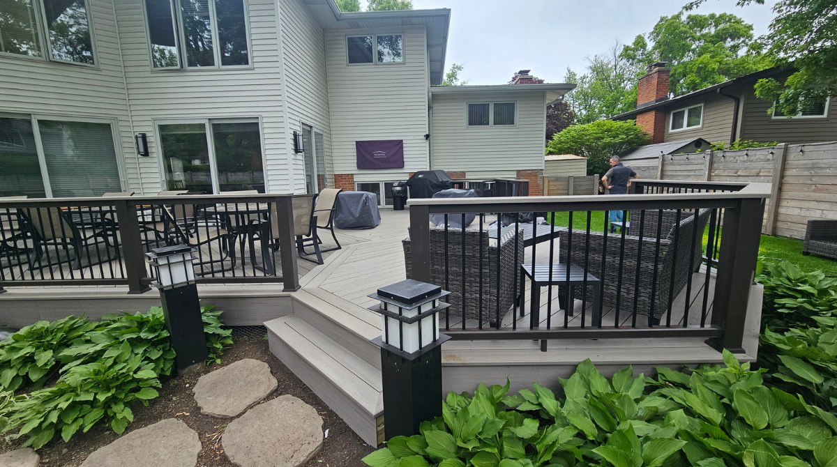 Backyard deck with black railings, steps, lantern, and sliding glass doors beside a house