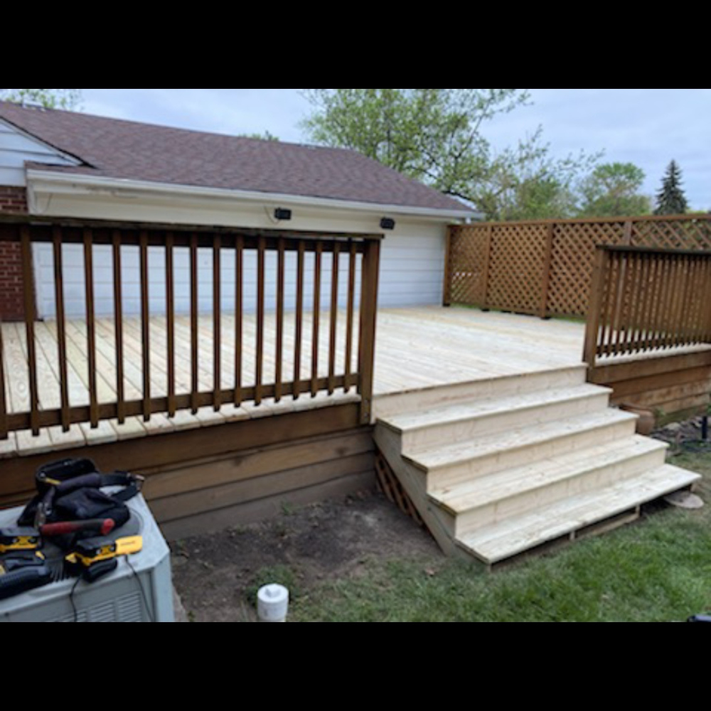Wooden backyard deck with white steps, brown railings, and a garage in the background