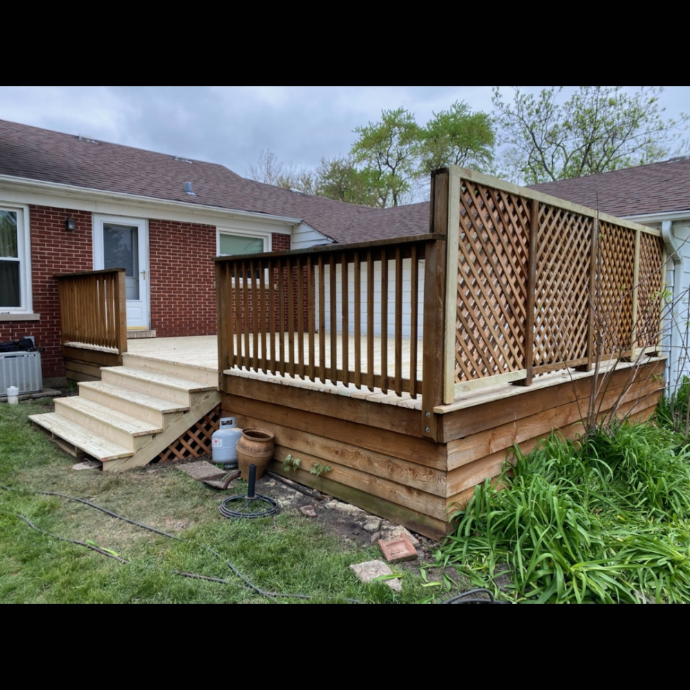 Wooden deck with lattice railing and stairs beside a brick house and grassy yard