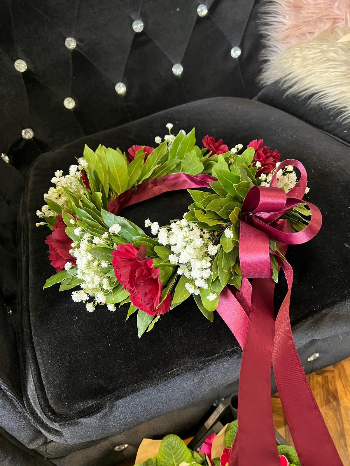 Corona floreale rossa e bianca con nastro rosa appoggiata su una sedia nera
