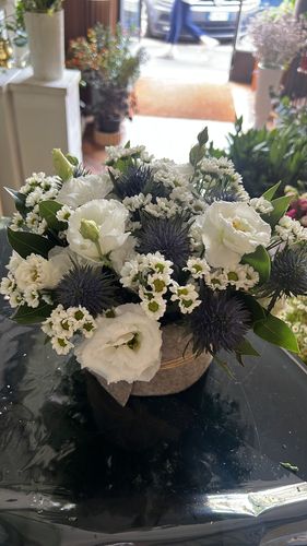 Mani che sistemano fiori bianchi su un cuscino color crema, appoggiato su un tavolo di legno in una stanza luminosa