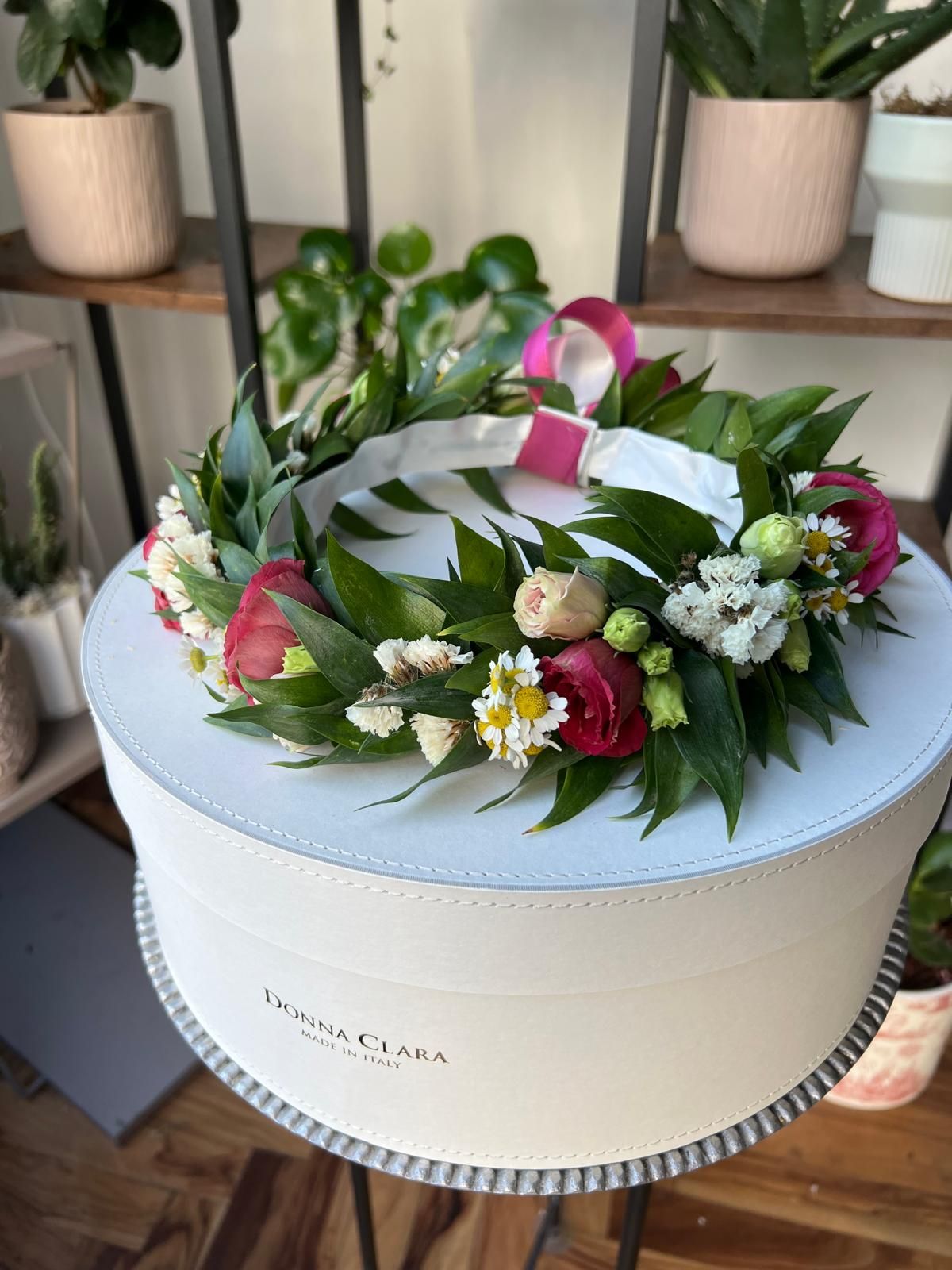Scatola regalo rotonda bianca, decorata con fiori rosa e bianchi e foglie verdi, su uno scaffale