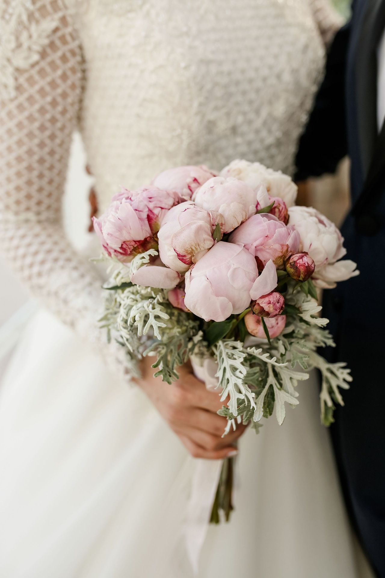Persona con un bouquet di peonie rosa pallido e fogliame accanto a un maglione color crema e a un vestito bianco
