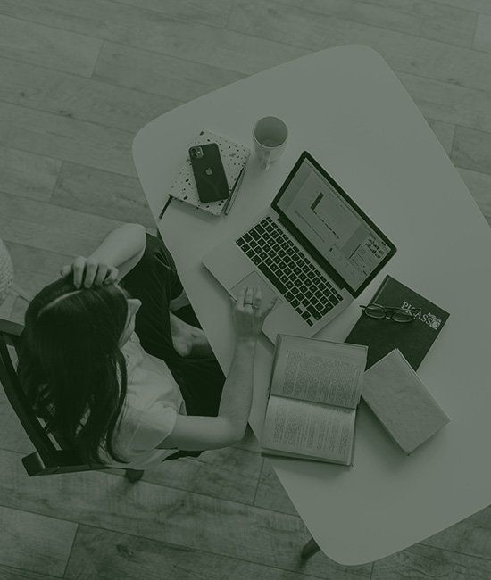 一位女士坐在辦公桌前，手裡拿著一台筆記型電腦和一本書。