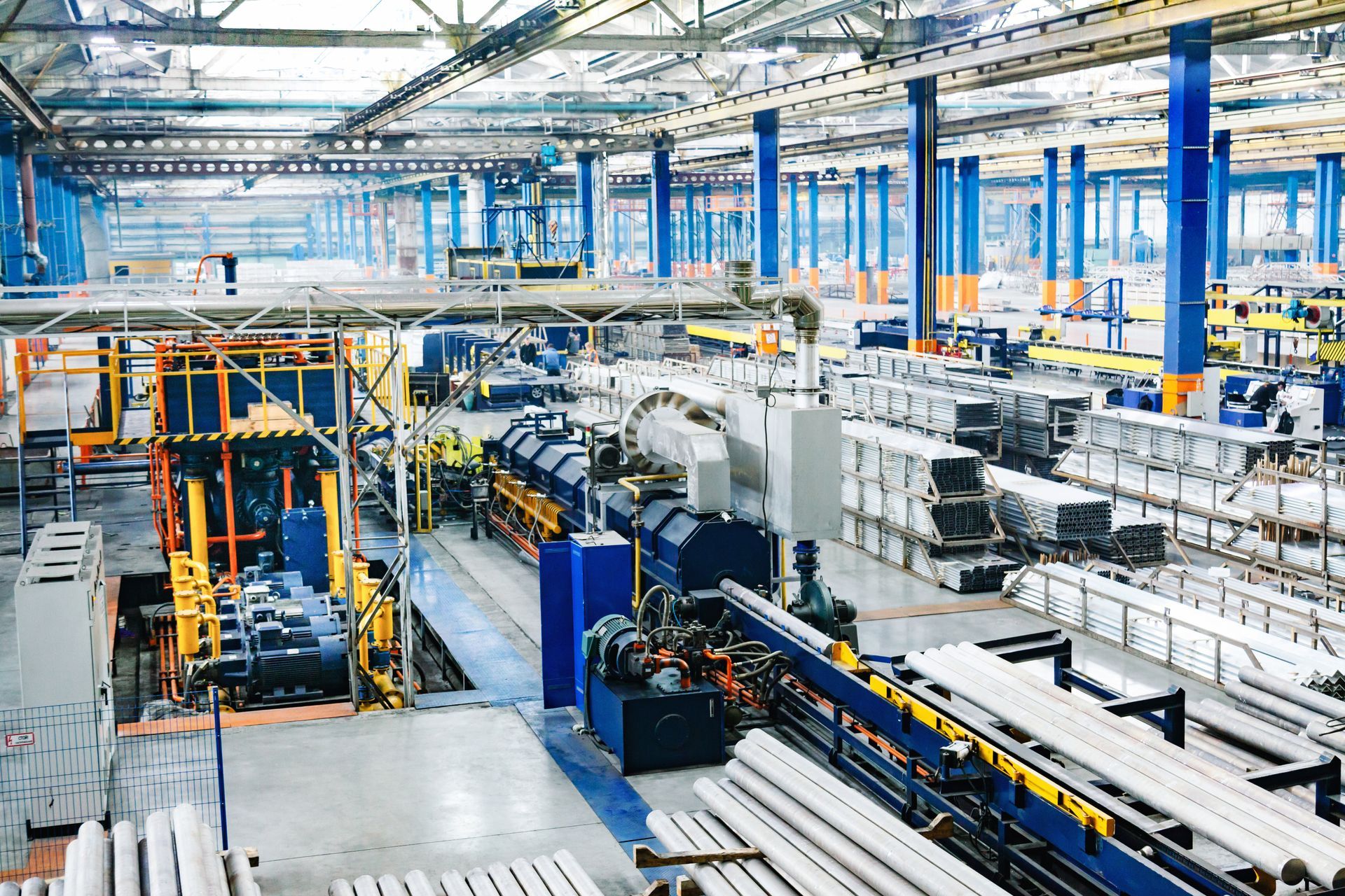 Factory interior with machinery and stacked metal pipes. Blue and gray tones.