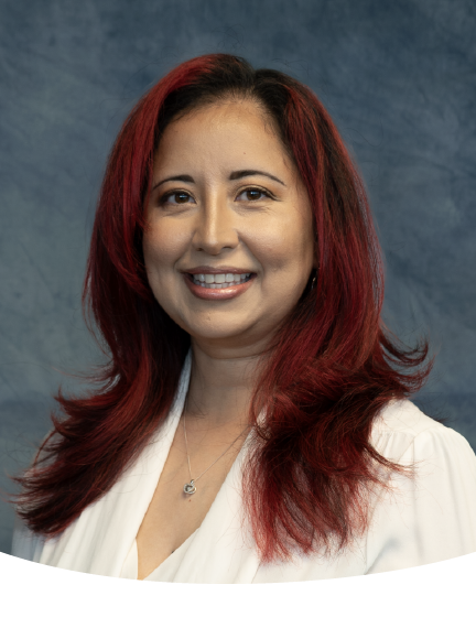 Woman with red-toned hair smiles, wearing a white top, against a blue backdrop.