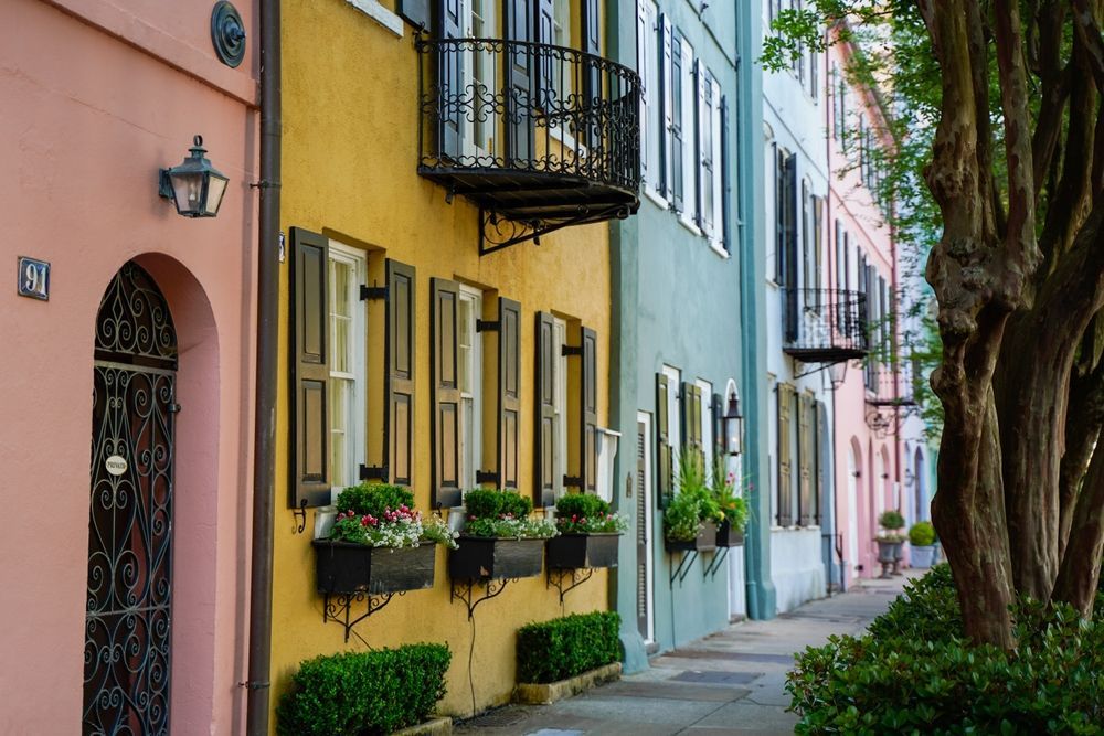Row of colorful historic houses with window boxes on a tree-lined street.