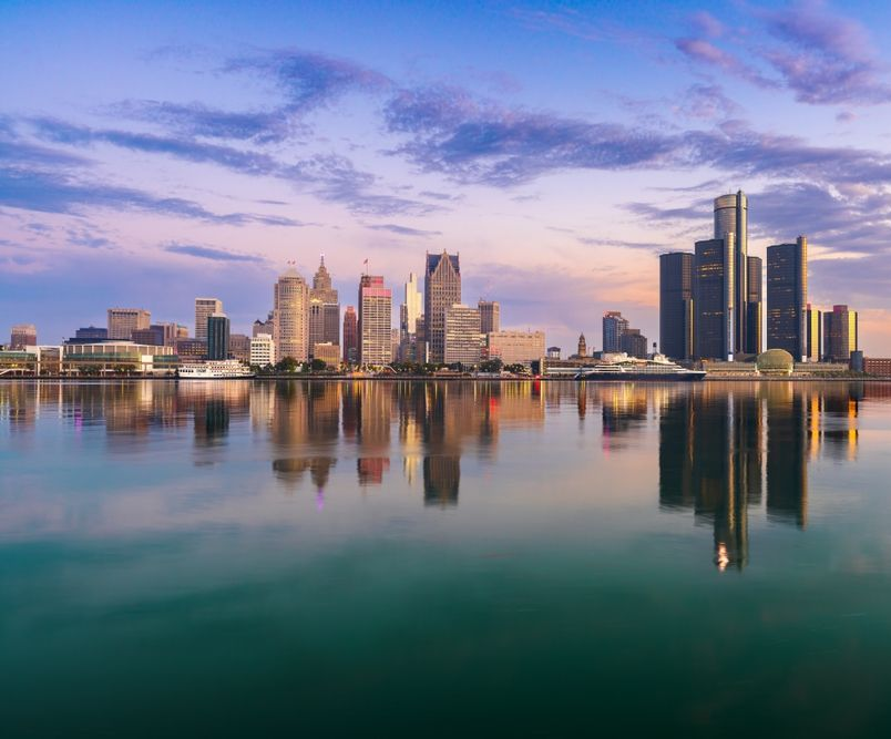 Detroit skyline reflecting in calm water at sunset.