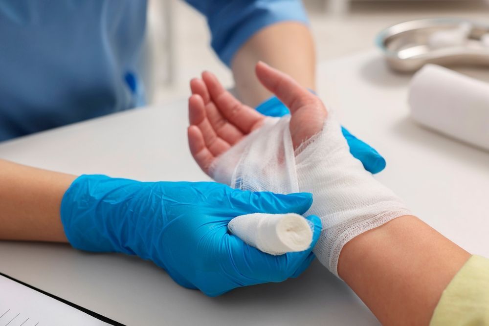 Gloved clinician bandaging a patient’s wrist with white gauze on a table